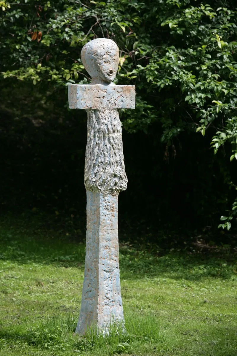 Vysoká světlá figura s hlavou nad příčným ramenem v zahradě