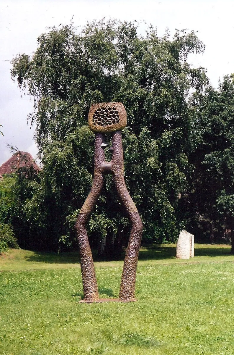 Hnědá figura s rozkročenýma nohama, které tvoří bránu