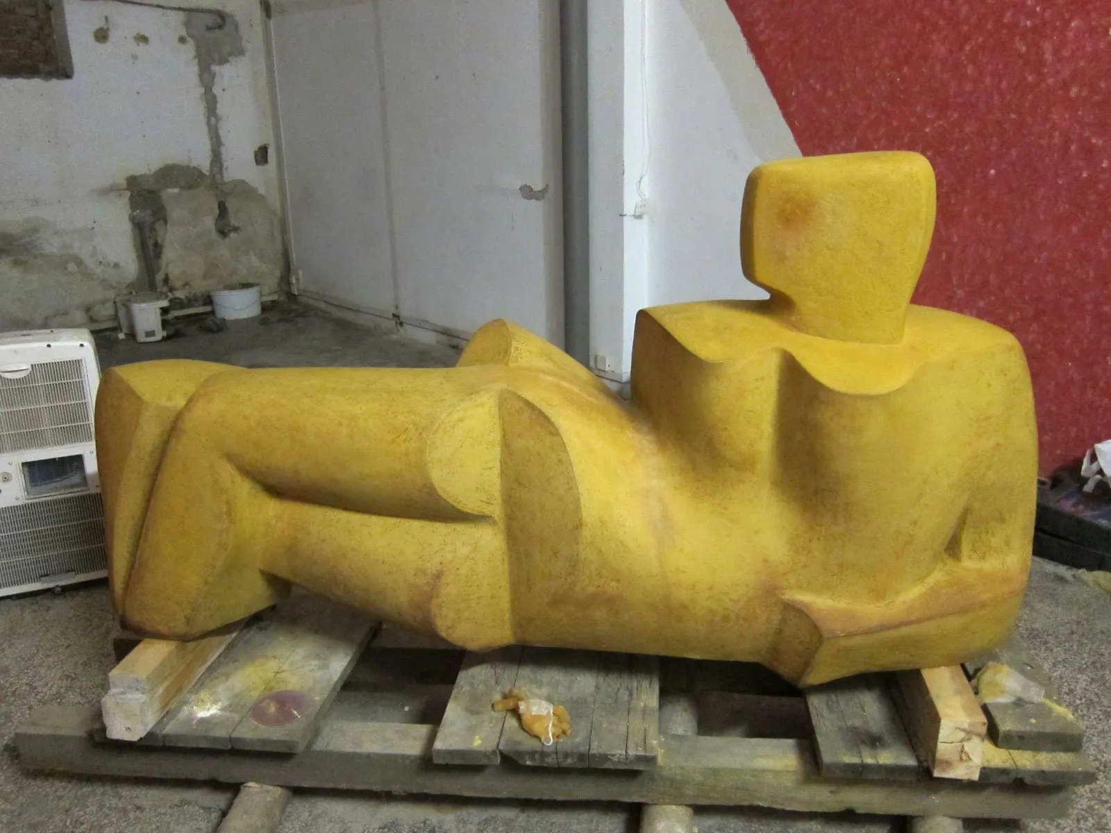 Žlutá kubizující ležící figura na paletách v dílně