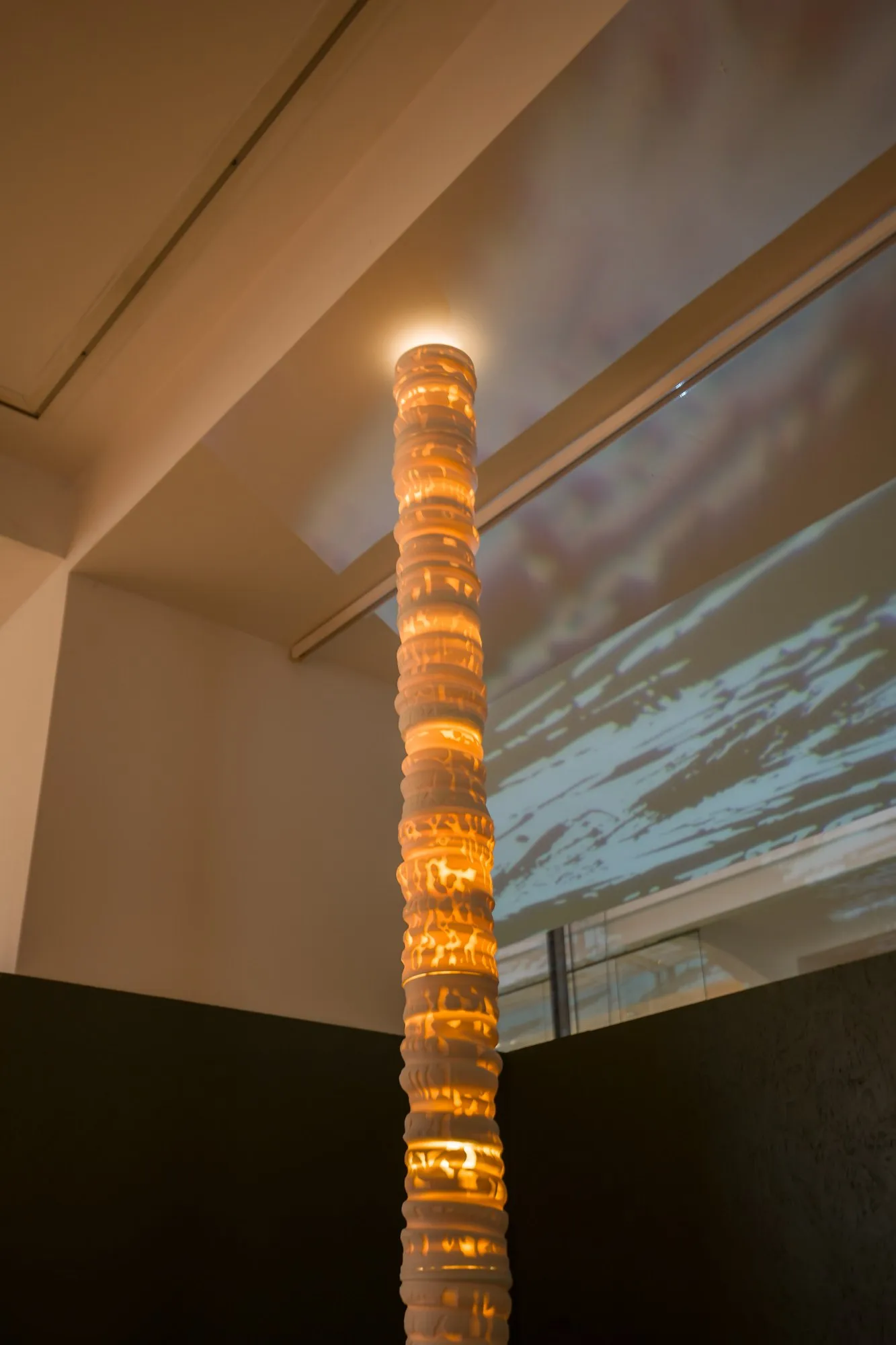 Svítící porcelánový sloup v galerii, na stěnu se promítá obraz