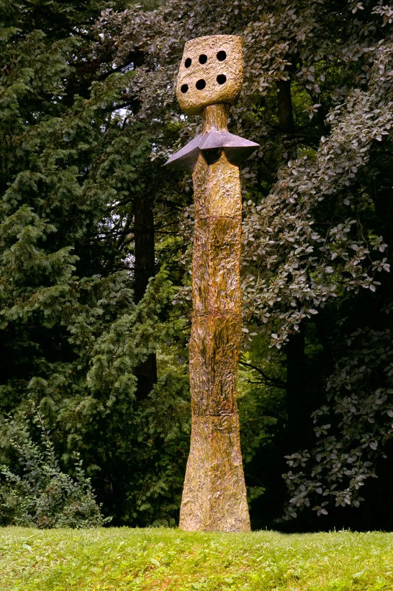 Vysoká štíhlá figura s děrovanou hlavou na trávníku