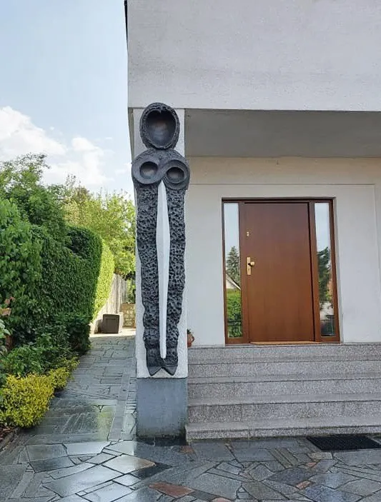 Tmavá plastika Strážce před vchodem, pohled z chodníku