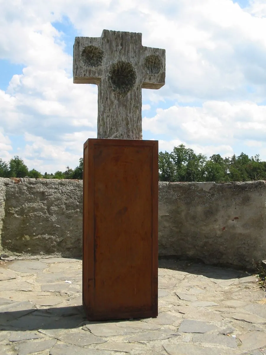 Kamenný kříž s kruhovými reliéfy na rezavém podstavci